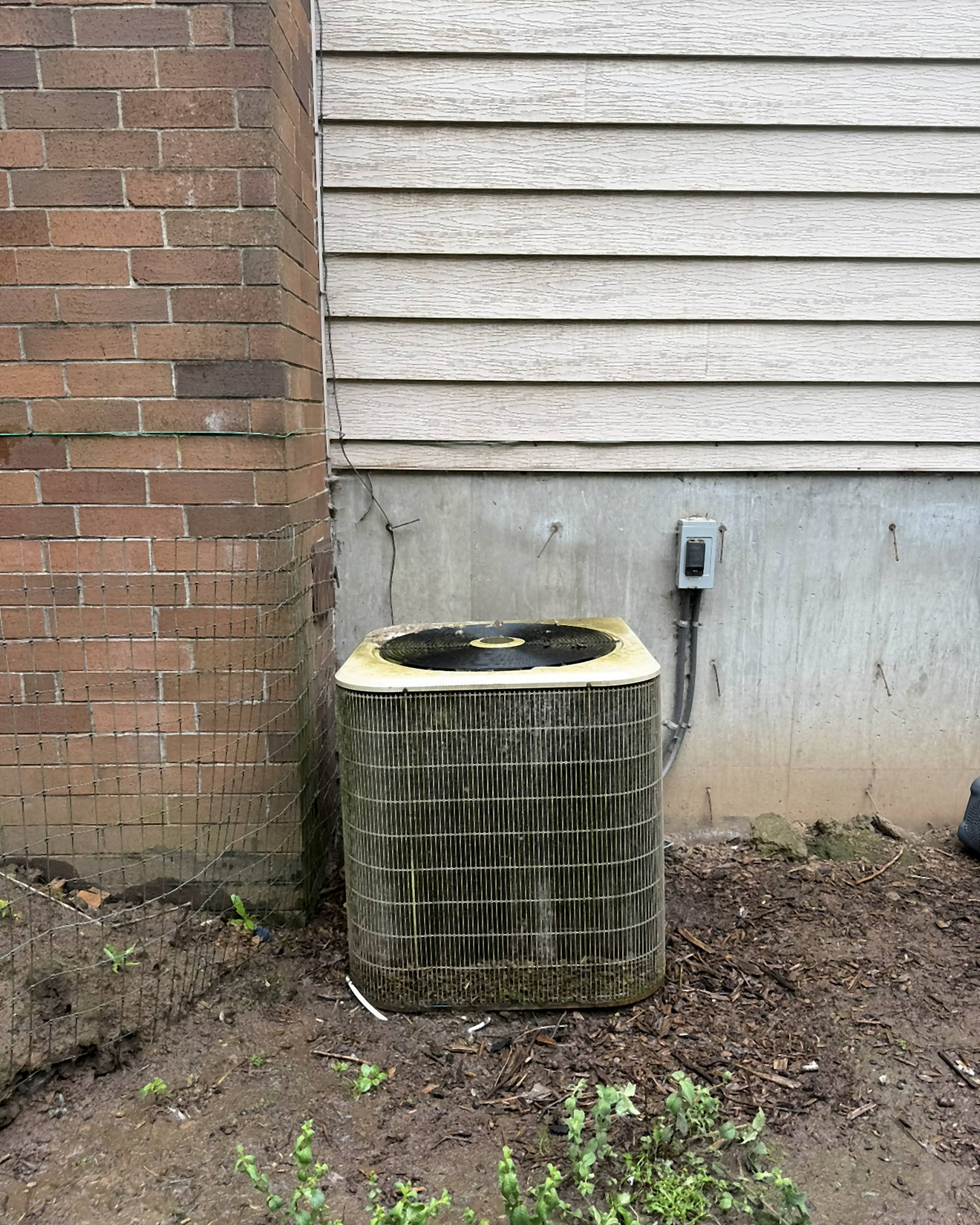 Before: old outdoor unit with an algae-covered coil sitting on bare dirt
